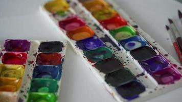 Brush takes different colors of watercolor paints from a palette and mixes them close-up video
