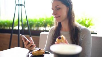 Frau Essen Eclairs im ein Cafe und mit ein Smartphone video