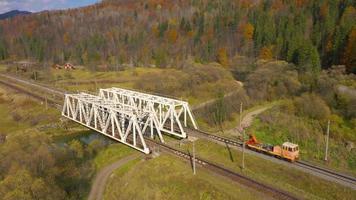 Aerial view of autumn mountain landscape - yellow forest, river, railway bridge and traffic on the road video