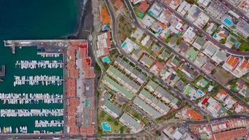 Top view on the coast of Tenerife - ocean, black sand beach, houses and hotels with pools, pier with boats, Canary Islands, Spain. video