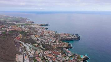 Top view on the coast of Tenerife - ocean, black sand beach, houses and hotels with pools, pier with boats, Canary Islands, Spain. video