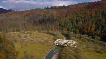 Aerial view of autumn mountain landscape - yellow forest, river, railway bridge and traffic on the road video