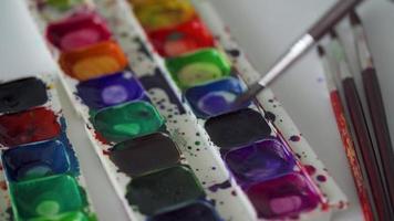 borsta tar annorlunda färger av vattenfärg målarfärger från en palett och blandar dem närbild video