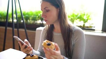 vrouw aan het eten eclairs in een cafe en gebruik makend van een smartphone video