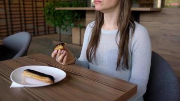 caucásico mujer comiendo chocolate eclair y Bebiendo café en un café video