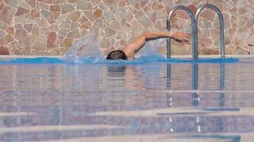 Man swims in a crawl style in the swimming pool in slow motion video