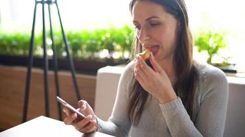 vrouw aan het eten eclairs in een cafe en gebruik makend van een smartphone video