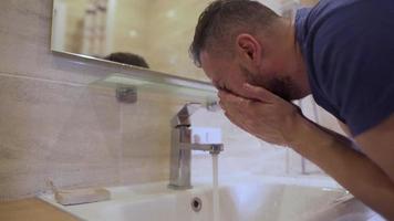 Bearded man washes his face with clean water in the bathroom. Morning hygiene. Slow motion video