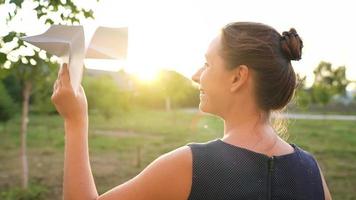 vrouw lanceert papier vliegtuig tegen zonsondergang achtergrond. concept van dromen over op reis of de beroep van een stewardess. video