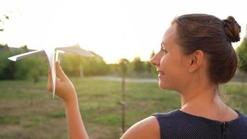 Woman launches paper airplane against sunset background. Concept of dreaming about traveling or the profession of a stewardess. video