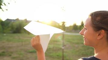 Woman launches paper airplane against sunset background. Concept of dreaming about traveling or the profession of a stewardess. video