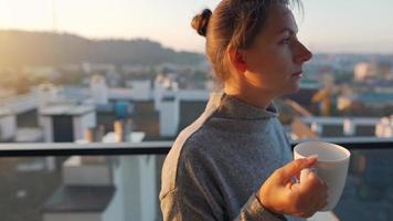 Frau beginnt ihr Tag mit ein Tasse von Tee oder Kaffee und Überprüfung E-Mails im ihr Smartphone auf das Balkon beim Dämmerung, schleppend Bewegung. modern städtisch Lebensstil video