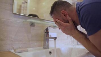 Bearded man washes his face with clean water in the bathroom. Morning hygiene. Slow motion video