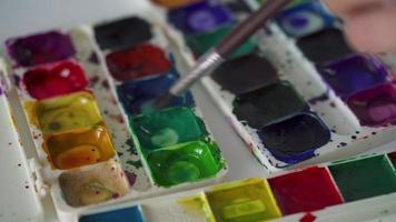 brosse prend différent couleurs de aquarelle des peintures de une palette et mélanges leur fermer video