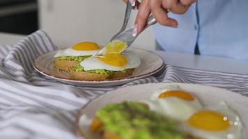 skivning rostat bröd med avokado och ägg. flytande äggula strömmande. friska vegan frukost. video