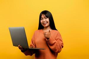 online communication concept asian girl use laptop at home yellow studio photo She is happy to spend her free time online while chatting with friends on social networks, shopping or working online.