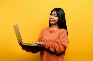 online communication concept asian girl use laptop at home yellow studio photo She is happy to spend her free time online while chatting with friends on social networks, shopping or working online.