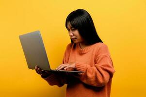 online communication concept asian girl use laptop at home yellow studio photo She is happy to spend her free time online while chatting with friends on social networks, shopping or working online.