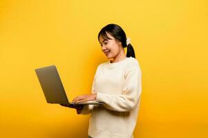 online communication concept asian girl use laptop at home yellow studio photo She is happy to spend her free time online while chatting with friends on social networks, shopping or working online.