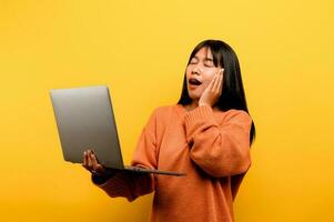 online communication concept asian girl use laptop at home yellow studio photo She is happy to spend her free time online while chatting with friends on social networks, shopping or working online.