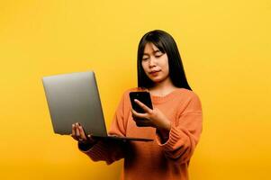 online communication concept asian girl use laptop at home yellow studio photo She is happy to spend her free time online while chatting with friends on social networks, shopping or working online.