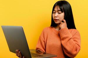online communication concept asian girl use laptop at home yellow studio photo She is happy to spend her free time online while chatting with friends on social networks, shopping or working online.