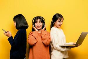 Three Asian women working with laptop and phone at the same time The two of them were communicating online and showing happy smiles. and listen to music around and friends concept online communication photo