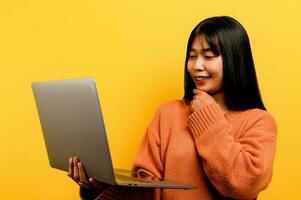 online communication concept asian girl use laptop at home yellow studio photo She is happy to spend her free time online while chatting with friends on social networks, shopping or working online.