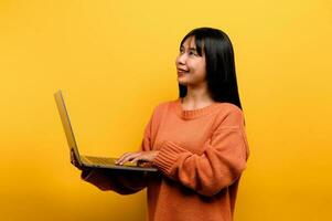 online communication concept asian girl use laptop at home yellow studio photo She is happy to spend her free time online while chatting with friends on social networks, shopping or working online.
