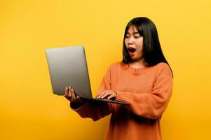 online communication concept asian girl use laptop at home yellow studio photo She is happy to spend her free time online while chatting with friends on social networks, shopping or working online.