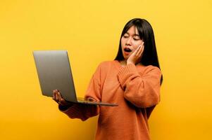 online communication concept asian girl use laptop at home yellow studio photo She is happy to spend her free time online while chatting with friends on social networks, shopping or working online.