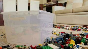 vistoso Lego juguete piezas y el plastico juguete caja, un montón de juguete Lego piezas en pie alrededor y Lego piezas arrojado dentro juguete caja, selectivo atención video