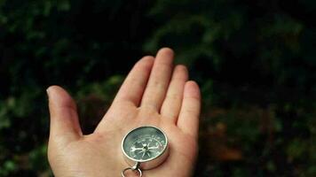 Person using forest compass moves by placing compass in hand, compass needle used in green forest moving and showing direction, selective focus video