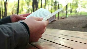 homme relaxant avec en train de lire livre dans forêt, homme séance sur banc tournant pages de livre, sélectif se concentrer, granuleux effet video