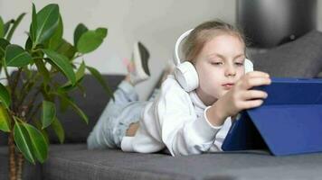 peu fille écoute à le la musique avec le écouteurs et numérique tablette. video