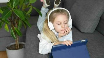 pequeño niña escuchando a el música con el auriculares y digital tableta. video