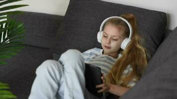 peu fille écoute à le la musique avec le écouteurs et numérique tablette. video