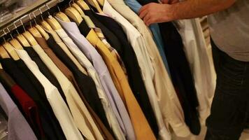 client à la recherche pour une chemise dans Vêtements magasin, chemises de différent couleurs accroché sur cintre dans boutique et homme choisir un vêtements, sélectif concentrer video