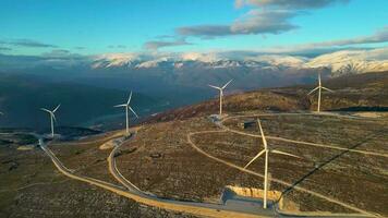 molinos de viento en las colinas durante la puesta de sol. energía renovable, energía verde. montañas en el fondo con nieve. energía eólica y respetuoso con el medio ambiente. Futuro sostenible. acabar con los combustibles fósiles. video