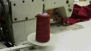 Tailor sewing red fabric in workshop, tailor using sewing machine with roll of red thread in workshop, selective focus video