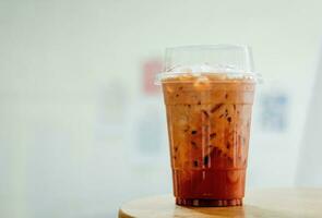 Thai tea, iced milk tea with milk in plastic cup on wooden table in coffee shop. photo