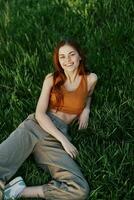 View from above a woman lying on the grass smiling and looking into the cameras happy lifestyle in the park on the green grass in the sunset light photo