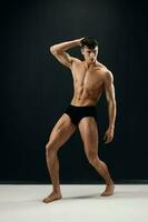 hombre con un mejorado muscular cuerpo en negro pantalones cortos posando en contra un oscuro antecedentes foto