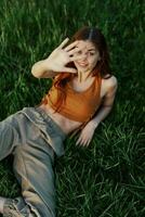 The view from above is a woman lying on the green grass in the park and relaxing in nature smiling and enjoying life. The concept of a healthy lifestyle photo