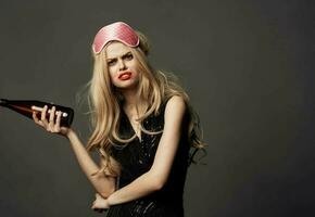 Indignant woman with a bottle of beer and a pink mask on the head of a blonde model photo