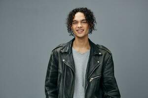 Cheerful smiling stylish tanned curly man leather jacket posing isolated on over gray studio background. Cool fashion offer. Huge Seasonal Sale New Collection concept. Copy space for ad photo