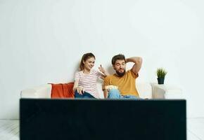 amigos hombre y mujer sentar en el sofá en frente de el televisión adentro y un flor en un maceta foto