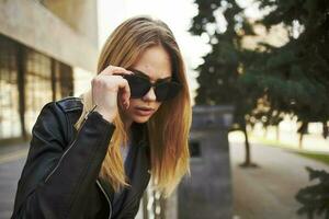 Fashionable woman glasses model leather jacket sun park building photo