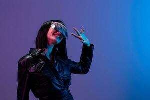 Friendly pretty awesome brunet woman in leather jacket trendy specular sunglasses greet someone posing isolated in blue violet color light background. Neon party Cyberpunk concept. Copy space photo