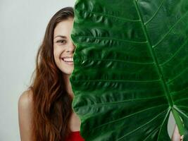 smiling pretty woman in swimsuit covers half of her face with palm leaf studio light background photo